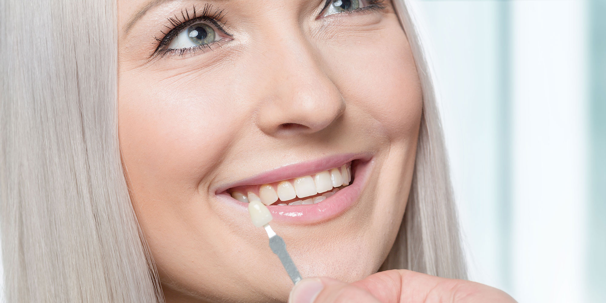 Using a shade guide at womans mouth to check veneer of tooth crown
