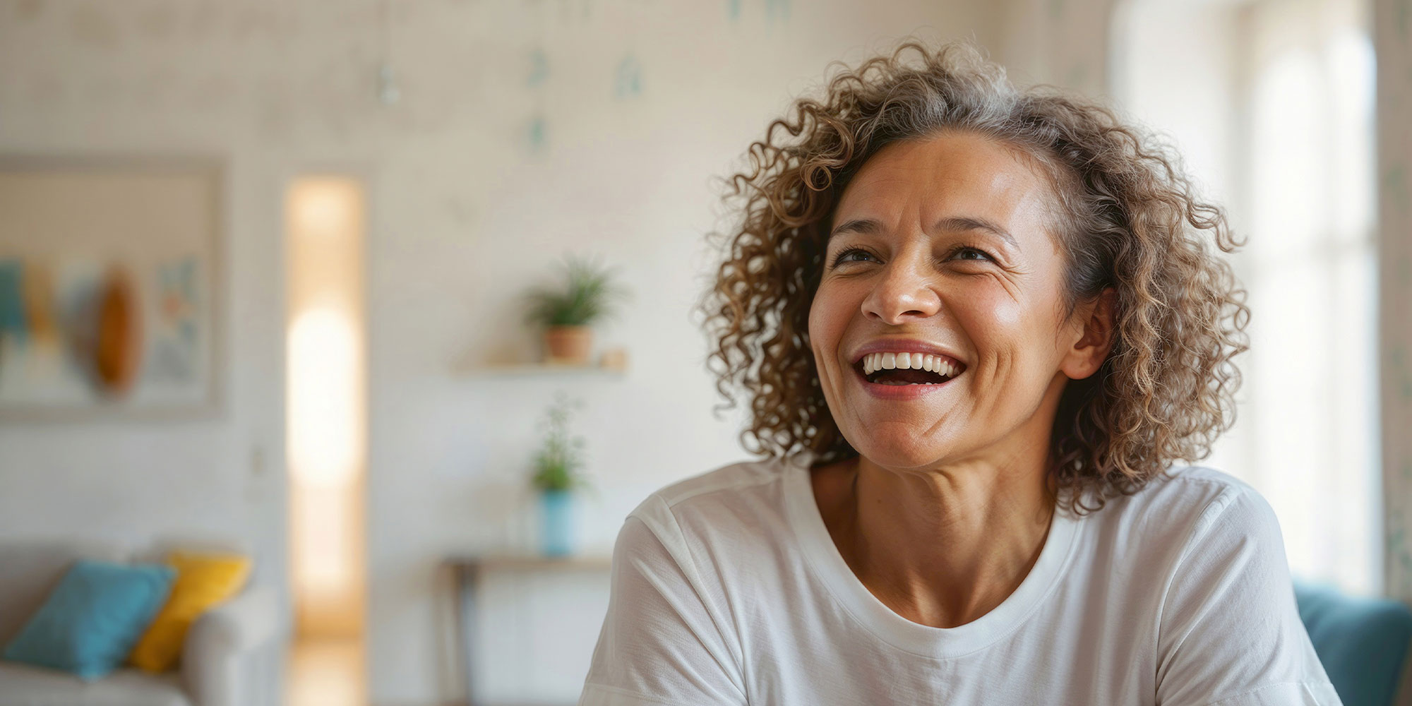 Portrait of happy mature African American woman in white t-shirt on blurred background of bright living room