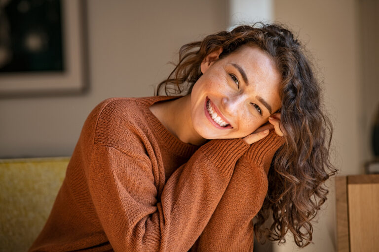 A friendly female dentist in Arlington, TX, Dr. Sarah Esmail, smiles reassuringly at a patient in a modern, sunlit dental office. No text on the image.