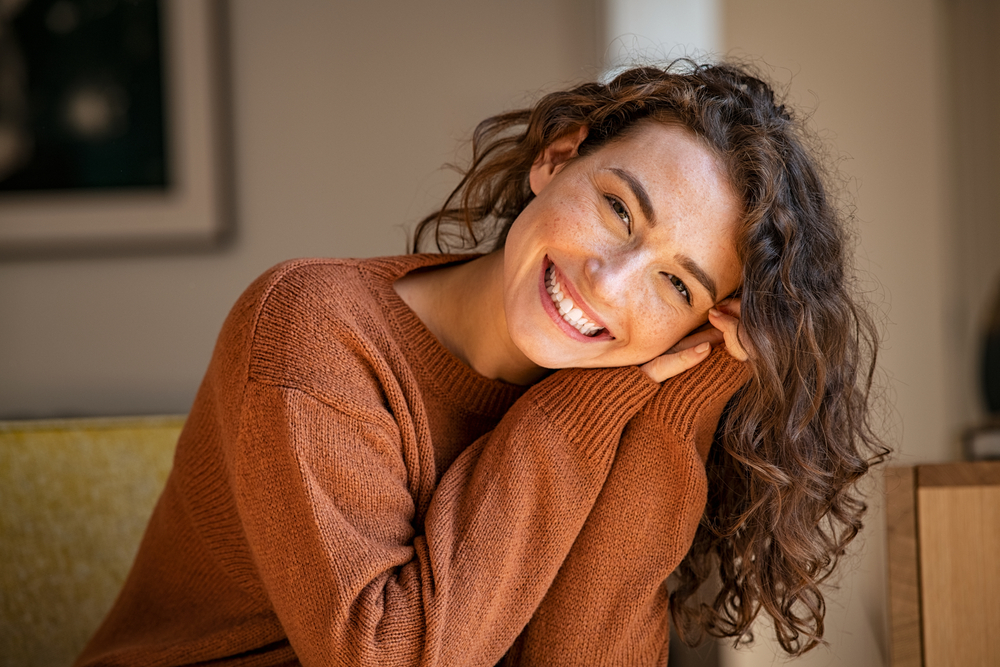 A friendly female dentist in Arlington, TX, Dr. Sarah Esmail, smiles reassuringly at a patient in a modern, sunlit dental office. No text on the image.